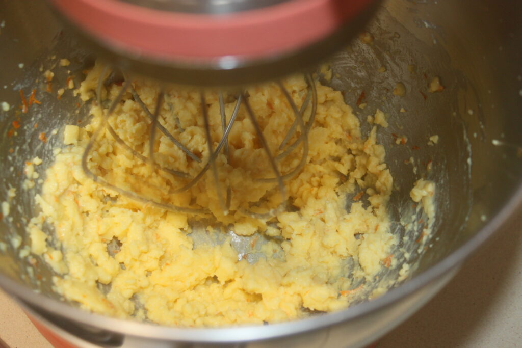 Un bol de mixeur contient un mélange de crème d'orange pour tartelettes jaune et épaisse avec un fouet, prêt à remplir de délicates tartelettes.