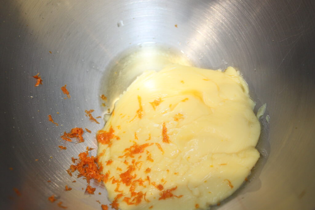 Dans un bol en métal, le beurre et le zeste d'orange se mélangent pour créer la garniture parfaite pour les tartelettes à la crème d'orange.