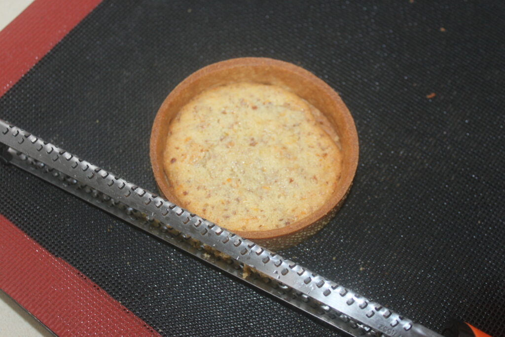 Une coque de Tartelettes à la crème d'orange, idéale pour confectionner des desserts exquis, repose sur un tapis de cuisson foncé à côté d'une râpe en métal brillante.
