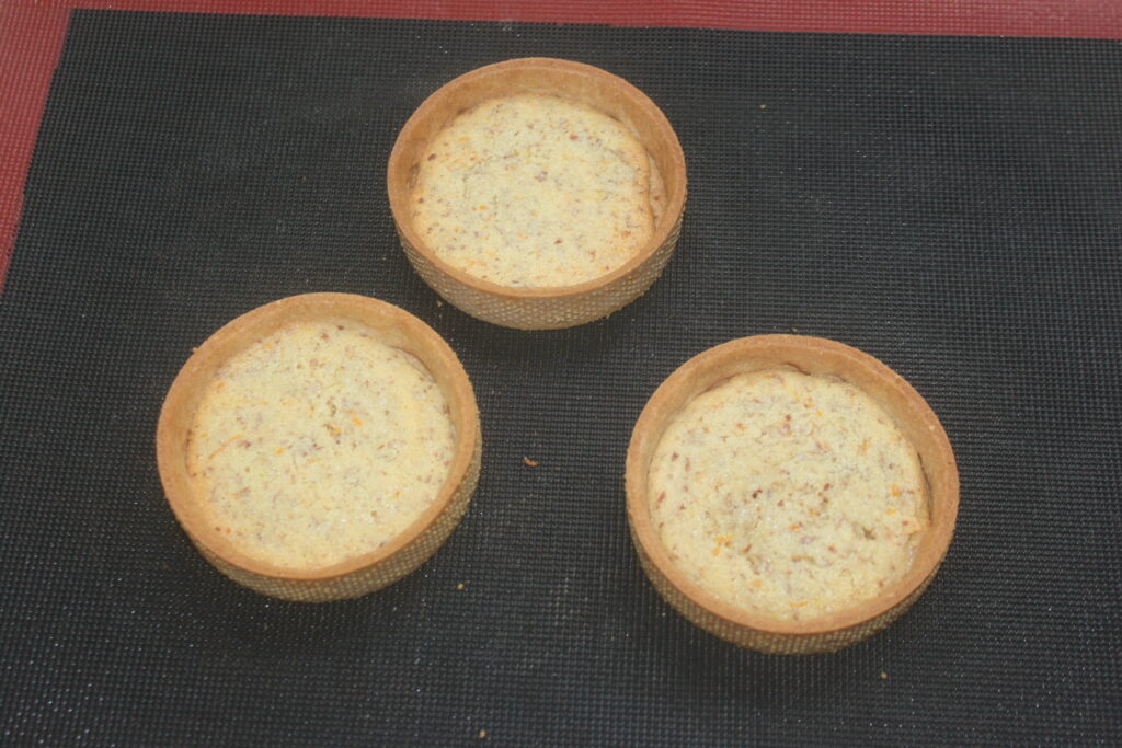 Trois coques de tartelettes crème d'orange vides reposent de manière invitante sur un tapis noir, parfait pour confectionner de délicieuses tartelettes.
