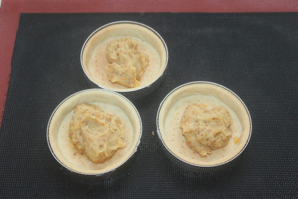 Trois tartelettes à la crème d'orange non cuites sont posées sur un tapis de cuisson noir, prêtes à se transformer en de succulentes tartelettes à l'orange.
