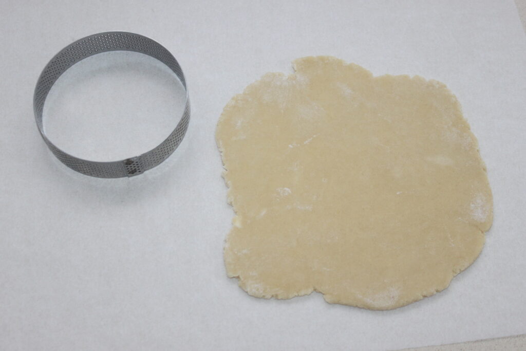 Un coupe pâte à tartelettes à la crème d'orange se trouve à côté de la pâte étalée sur une surface blanche, préparée pour fabriquer des tartelettes idéales remplies de délicieuse crème d'orange.