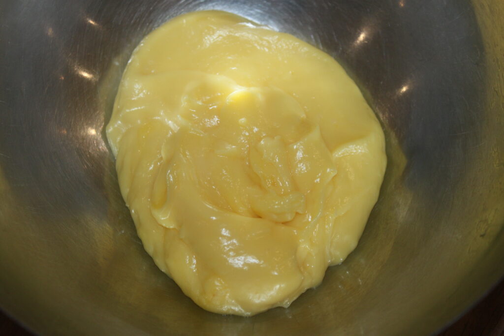 Un bol en métal contient un mélange de crème d'orange jaune et soyeux, idéal pour garnir les tartelettes à la crème d'orange.