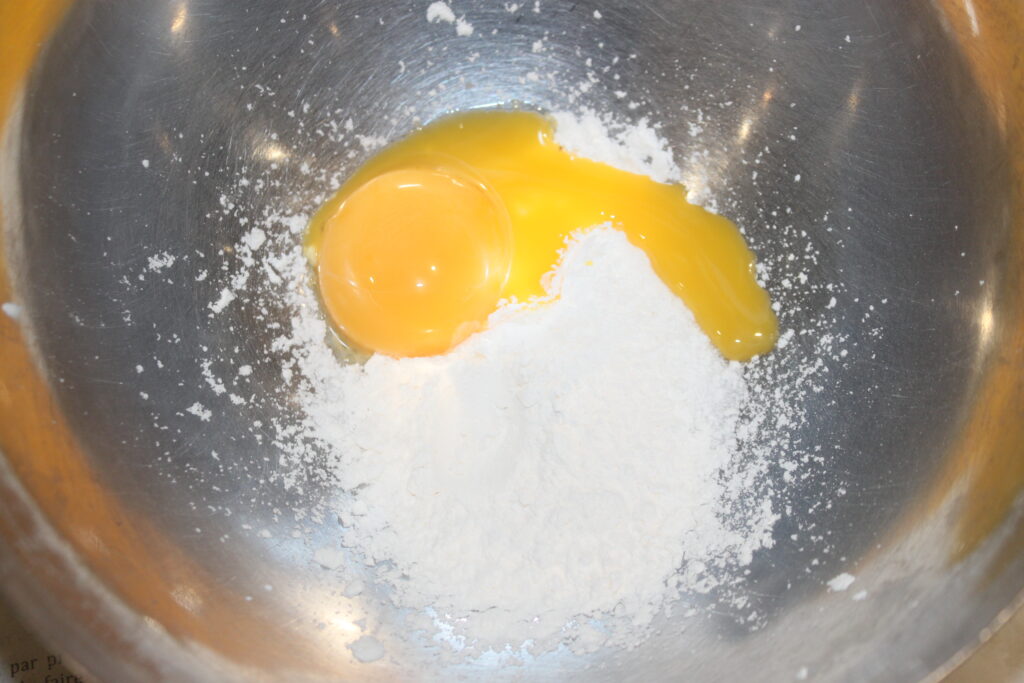 Un œuf cassé et de la farine sont dans un bol en métal, prêts à créer de délicieuses Tartelettes à la crème d'orange.