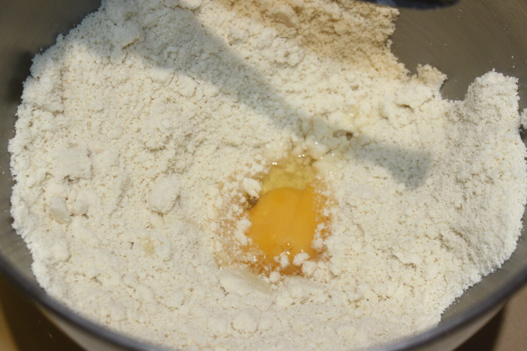 Un œuf cassé niché dans de la farine dans un bol à mélanger est parfait pour faire des tartelettes à la crème d'orange.