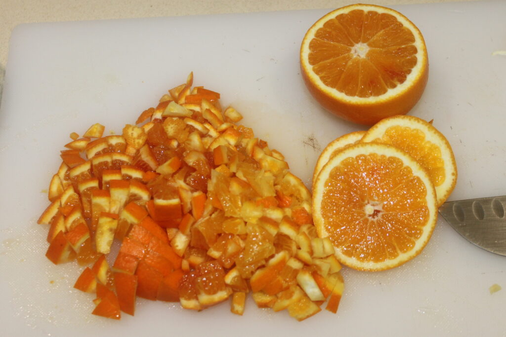 Orange hachée et tranchée sur une planche à découper blanche avec un couteau, prête à ajouter une explosion de fraîcheur à vos Tartelettes crème d'orange.