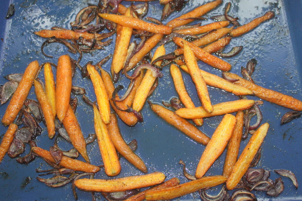 Savourez la délicieuse combinaison de carottes rôties et d'oignons rouges tranchés sur une plaque à pâtisserie bleue, parfaite pour accompagner le chèvre frais.