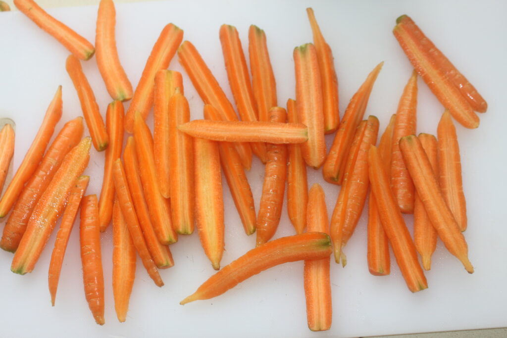Des carottes miniatures tranchées, rappelant les teintes vibrantes d'une tarte tatin, sont dispersées sur une planche à découper blanche immaculée.