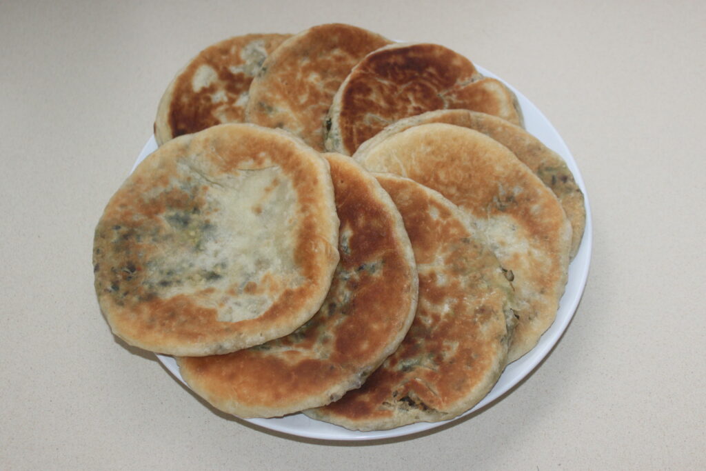Une assiette de galettes rondes et dorées disposées en pile sur une surface de couleur claire, parfaites pour accompagner des garnitures salées ou un accompagnement de tofu mariné.