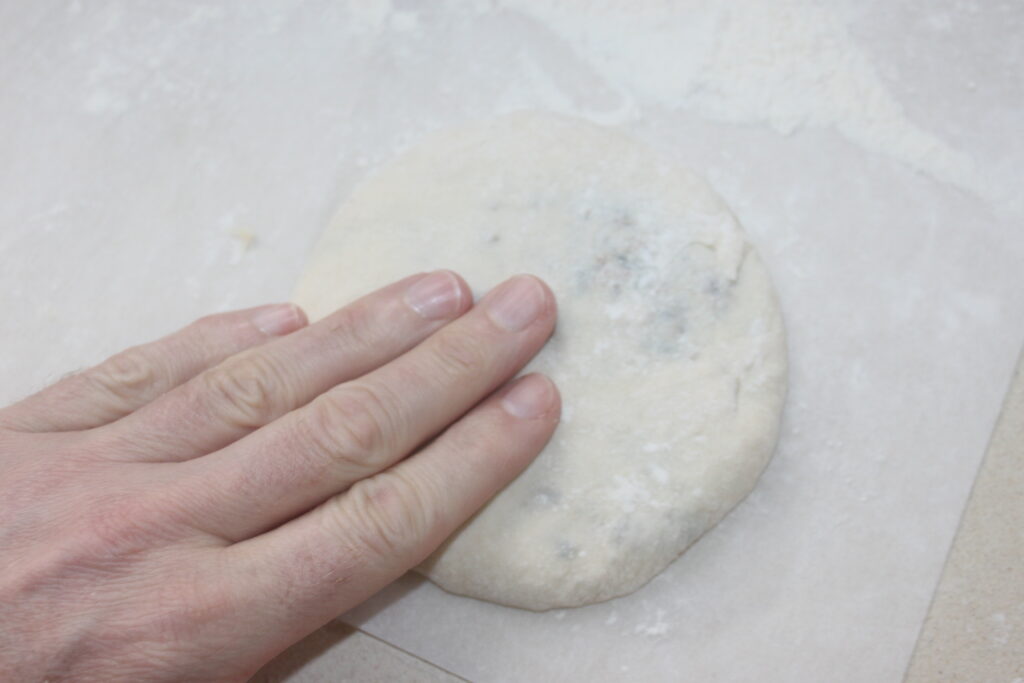 Une main appuie sur un morceau de pâte rond, se préparant à créer de délicates galettes sur une surface farinée.