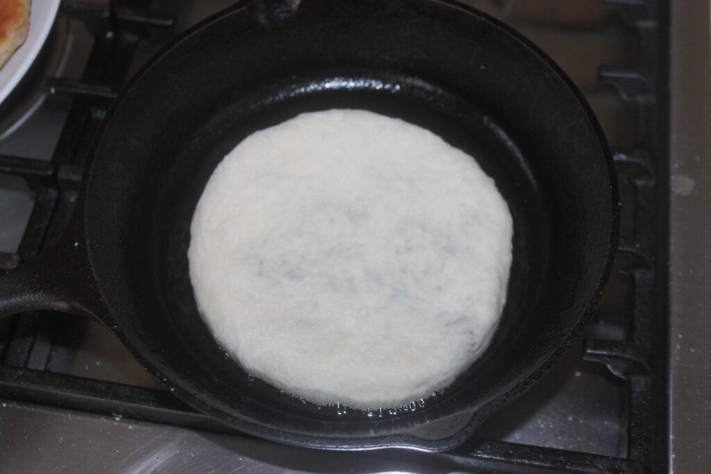 Un morceau de pâte rond qui grésille aux côtés de shitakés dans une poêle noire sur une cuisinière.