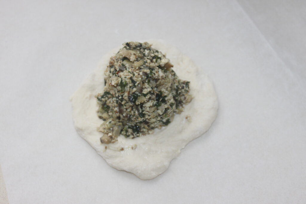 Une délicieuse galette dont la pâte est garnie d'un mélange vibrant de légumes hachés, de céréales et de shitakés savoureux, reposant élégamment sur une surface blanche.