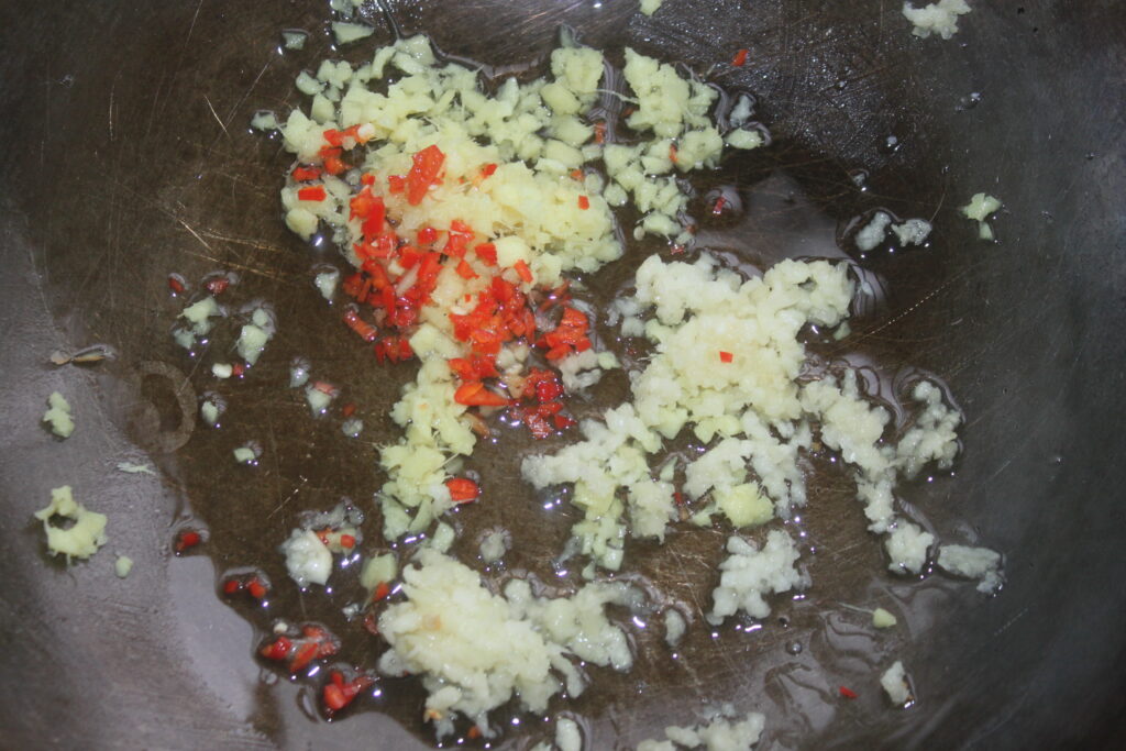 L'ail haché, le gingembre et le piment rouge grésillent dans une poêle avec de l'huile, tandis que les shitakés savoureux ajoutent une profondeur terreuse au mélange.