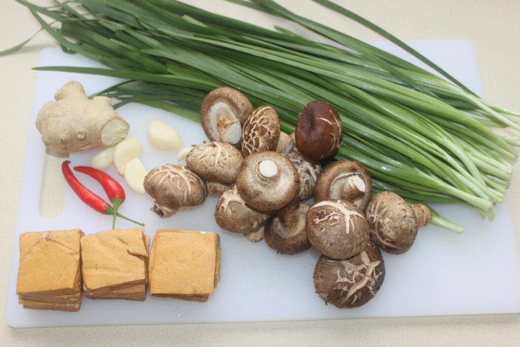 Une planche à découper avec du tofu, des champignons shiitake, des gousses d'ail, du gingembre, des piments et des oignons verts prêts à créer un délicieux repas lahé.