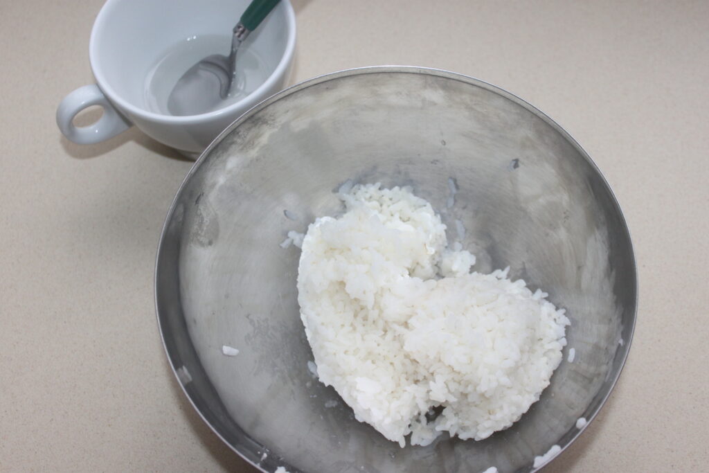 Un bol de riz blanc cuit à côté d'une tasse avec une cuillère.