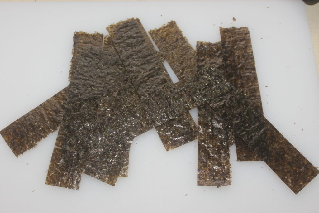Plusieurs bandes rectangulaires d’algues nori séchées sont disposées sur une surface blanche.