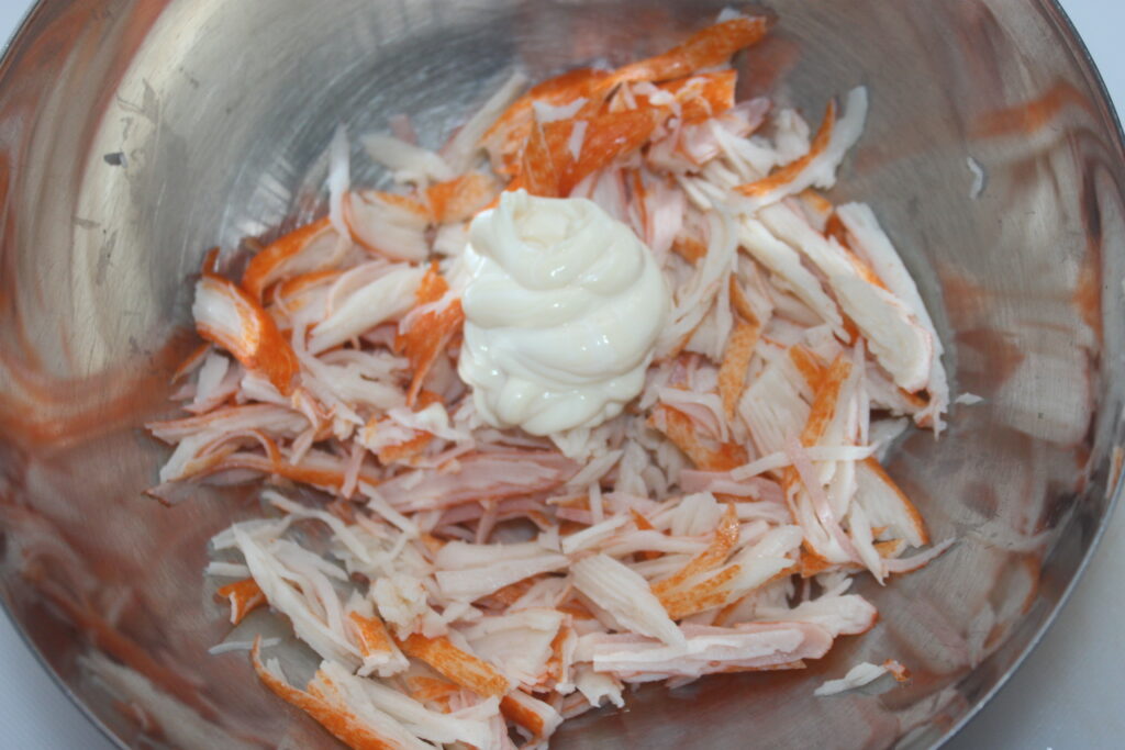 Bâtonnets de crabe râpés et une cuillerée de mayonnaise dans un bol en acier inoxydable.
