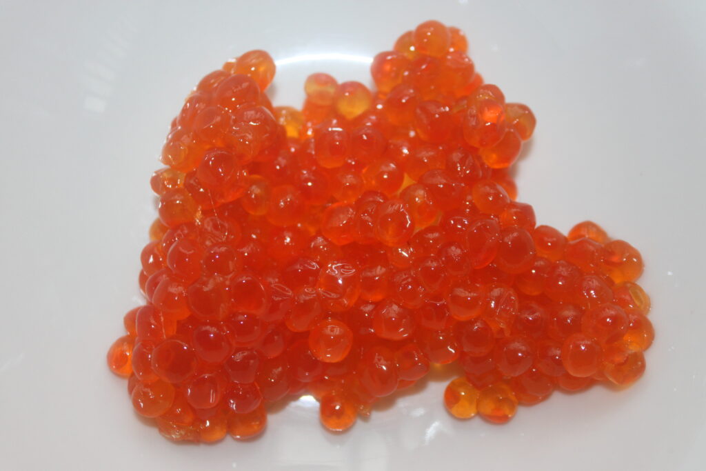 Un tas d'œufs de poisson orange sur une assiette blanche.