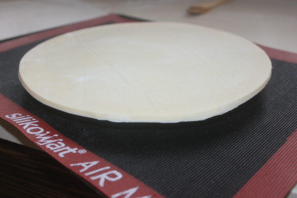 Un morceau de pâte rond et plat saupoudré d'une pointe de caramel est placé sur un tapis de cuisson en silicone, prêt à être cuit.