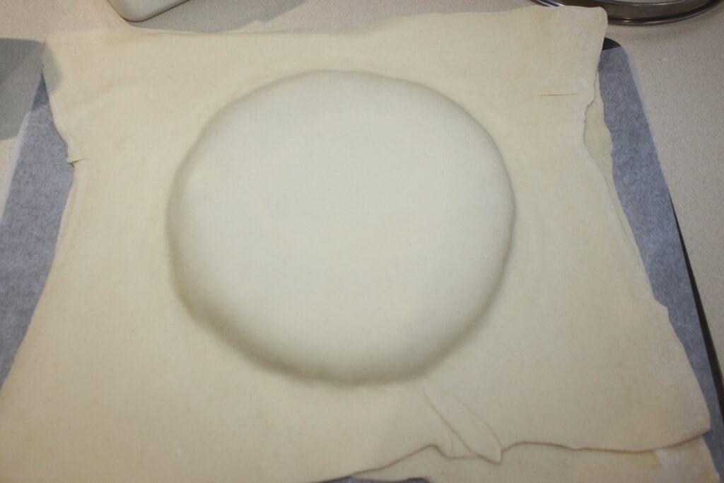 Une feuille de pâte feuilletée avec un monticule rond en dessous est posée sur une plaque à pâtisserie, rappelant une galette des Rois invitante remplie de caramel.