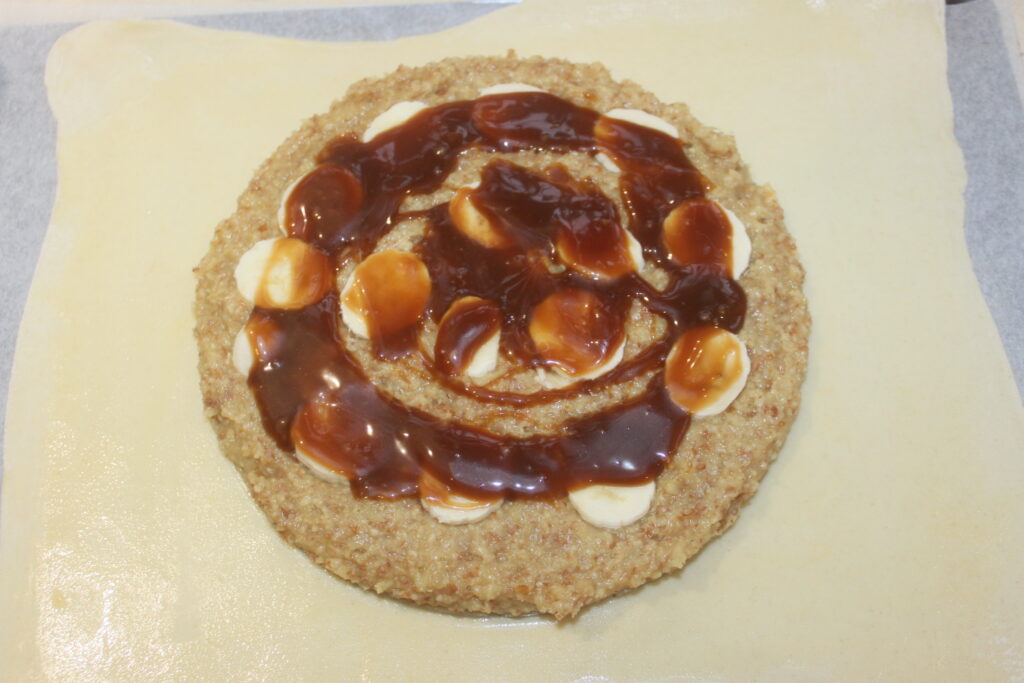 Un mélange rustique de pâte feuilletée crue recouverte de poudre d'amandes, de bananes mûres et d'un filet de sauce au caramel crée une délicieuse touche rappelant une galette des Rois.