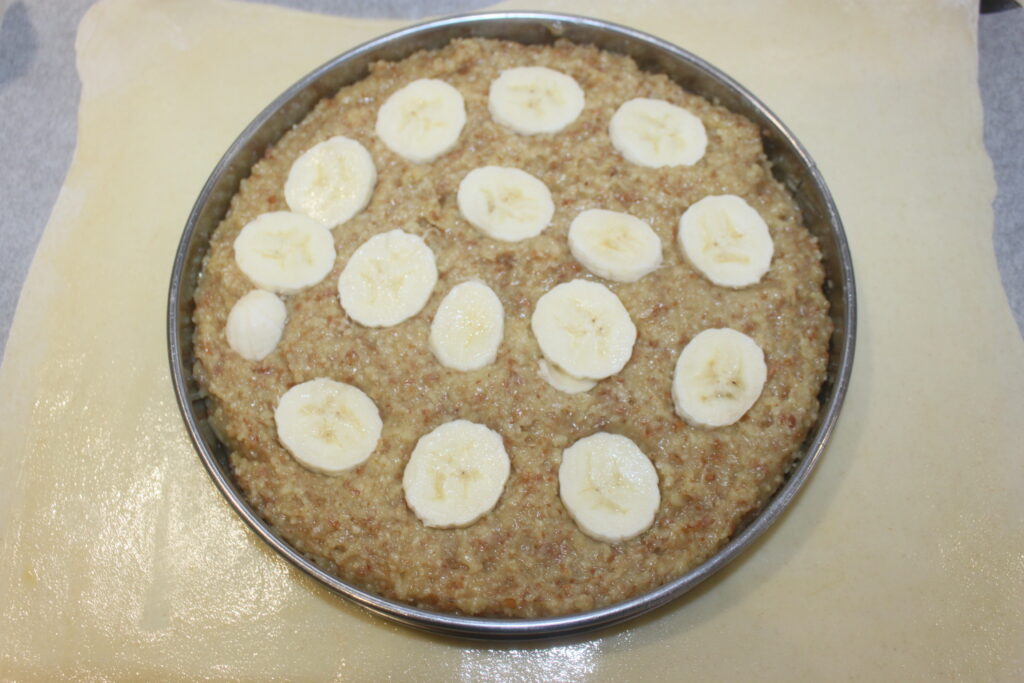 Un plat de cuisson rond contient un mélange de céréales, orné de tranches de bananes et d'un soupçon de caramel, le tout posé sur une délicate feuille de pâte.