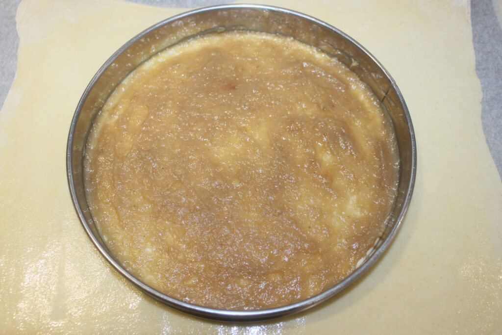 Un moule rond rempli d'un mélange de caramel brun clair et lisse, posé sur une feuille de pâte feuilletée étalée, rappelant une galette des Rois classique.