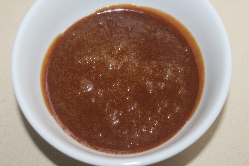 Un bol blanc rempli de sauce au caramel, présentant une surface brillante et de petites bulles.