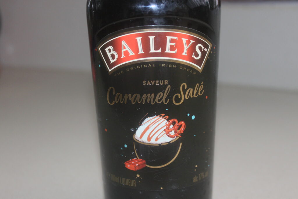 Une bouteille de liqueur de crème irlandaise au caramel salé Baileys orne une surface neutre, sa riche saveur de caramel rappelant une galette des rois décadente.