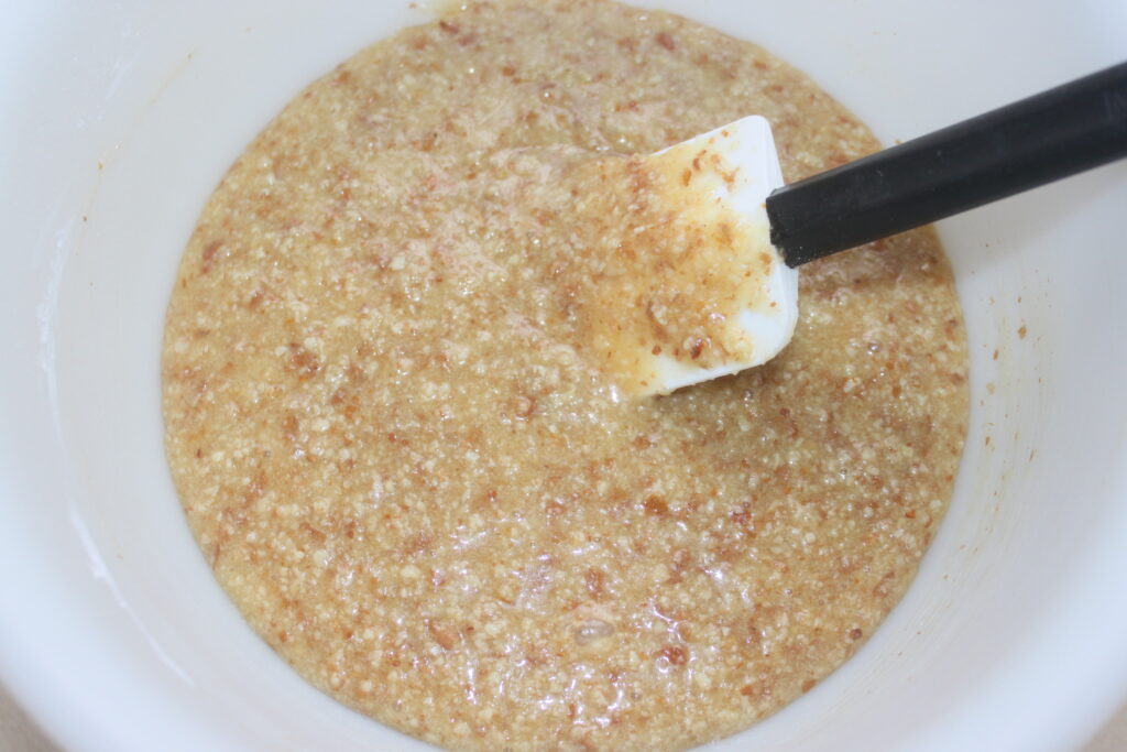 Un bol blanc contient un mélange brun grossier de cacahuètes écrasées, avec une spatule posée à l'intérieur.