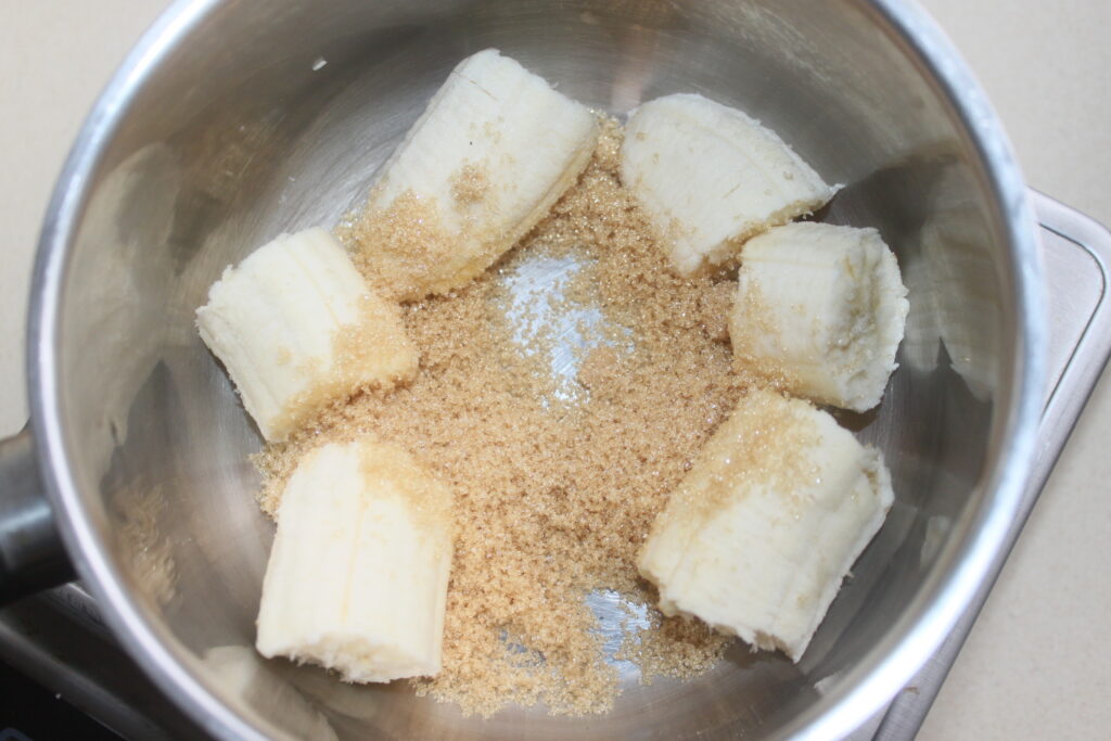 Des bananes tranchées, un soupçon de saveur de banane et de cassonade se mélangent harmonieusement dans un bol en métal.