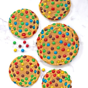 Six biscuits parsemés de mini M&M's vibrants sont dispersés sur une surface en marbre blanc, créant une délicieuse touche de couleur.