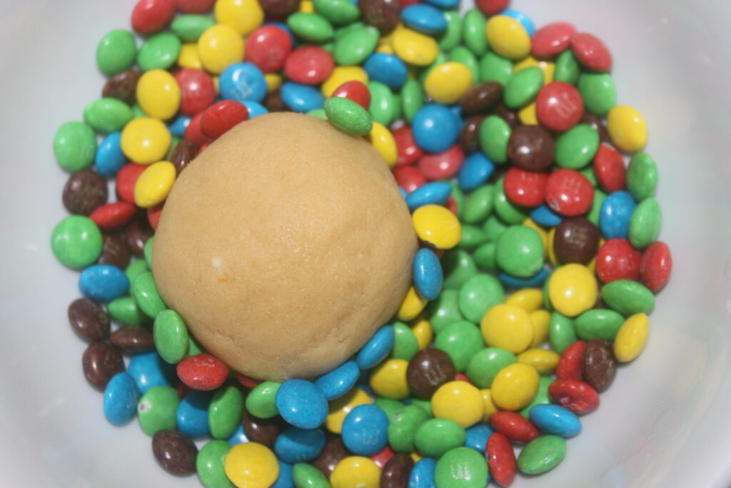 Une boule de pâte entourée de mini M&M's colorés offre une délicieuse friandise, parfaite pour fabriquer des biscuits dans un bol.