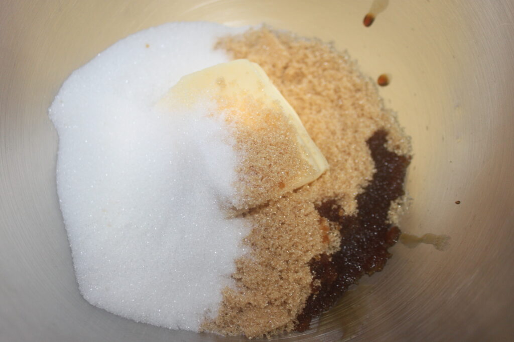 Un bol à mélanger contenant du sucre blanc, du sucre brun, de l'extrait de vanille et du beurre attend d'être transformé en délicieux biscuits avec des mini M&M's colorés.