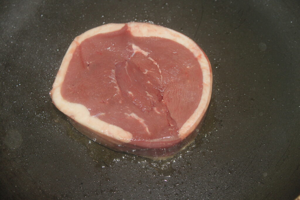 Un steak rond cru avec un anneau de graisse blanche est cuit dans une poêle, son arôme riche se mêlant aux morilles terreuses pour créer une symphonie culinaire alléchante.