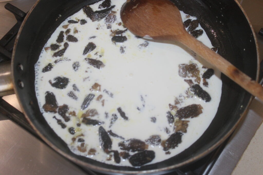 Une casserole sur le feu contient un liquide crémeux avec des morceaux de cèpes noirs, remués doucement avec une cuillère en bois.