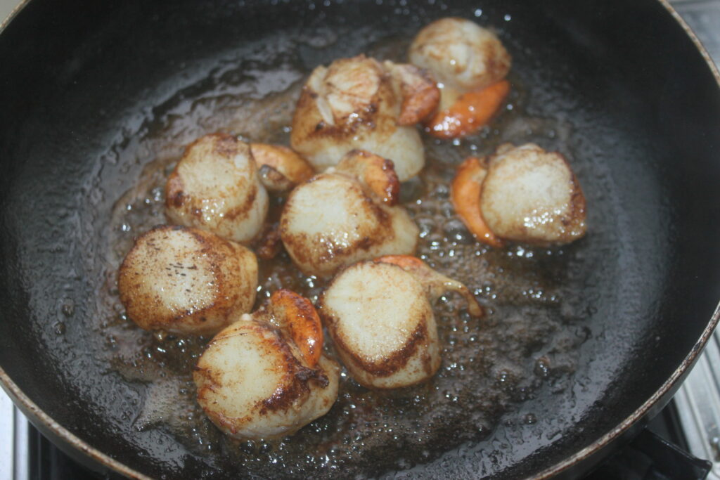 Les coquilles Saint Jacques saisies dans une poêle chaude avec de l'huile, présentant un extérieur parfaitement doré, sont rehaussées d'une touche de beurre à l'orange.