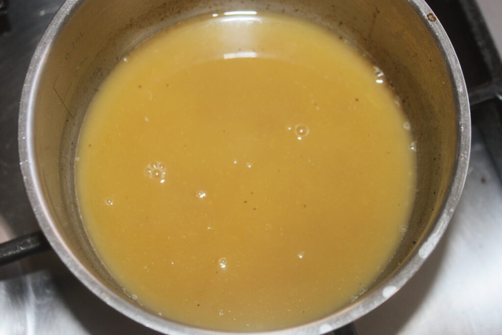 Une casserole remplie d'un liquide jaunâtre, rappelant le beurre à l'orange, mijote doucement sur le feu, peut être un bouillon savoureux en préparation.