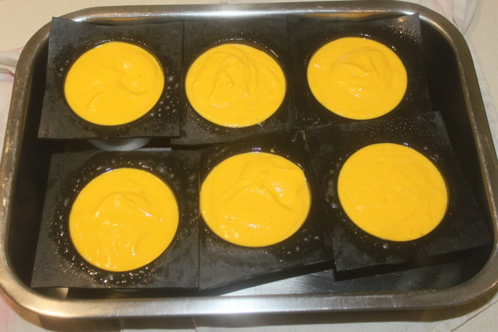 Six moules ronds remplis d'une pâte jaune onctueuse, laissant entrevoir la riche essence du potimarron, sont placés dans un plateau en métal.