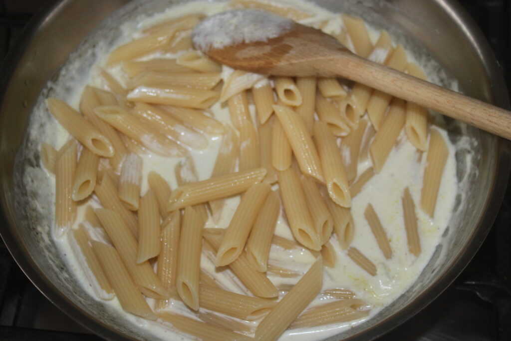 Les pâtes penne sont des pâtes frites dans une sauce riche au gorgonzola avec une cuillère en bois dans une casserole.