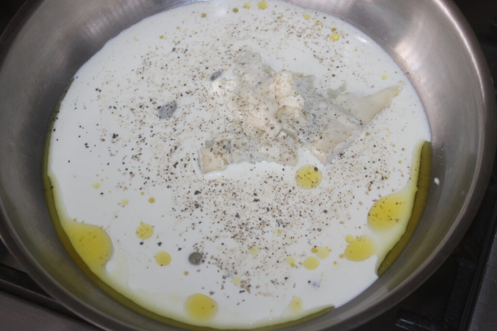 Une poêle avec de la crème, de la sauce gorgonzola et du poivre noir en préparation d'un plat délicieux.