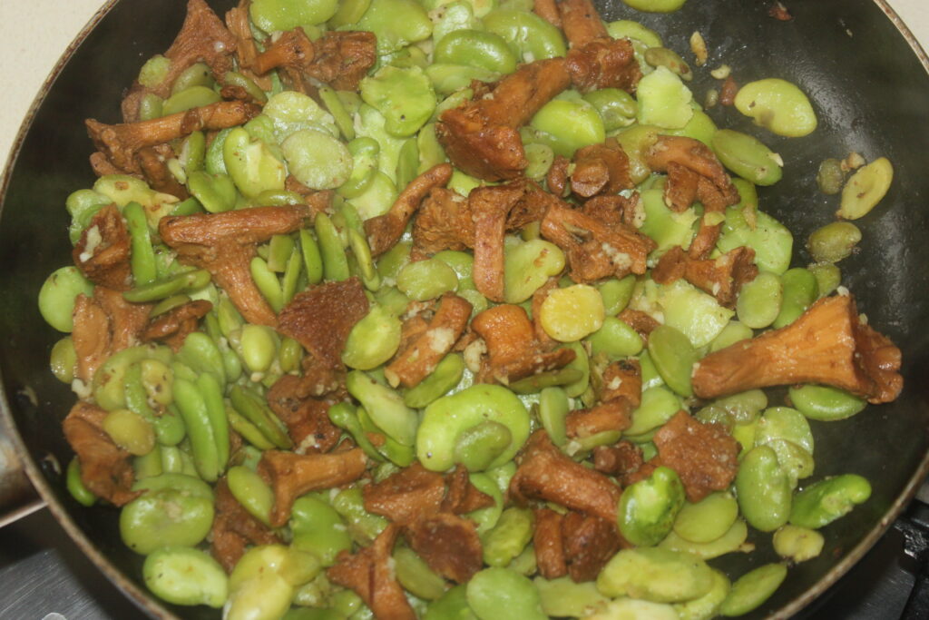 Une poêle remplie de girolles et de fèves vertes sautées.