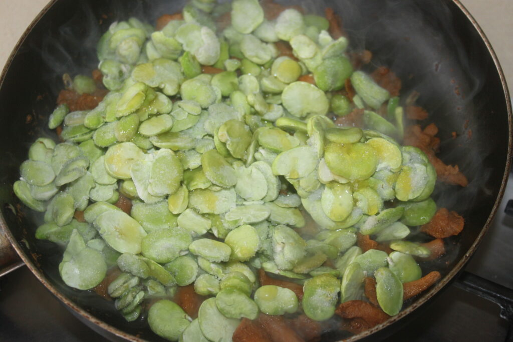 Une poêle de fèves surgelées cuites avec de la viande hachée et une touche de gorgonzola crémeux fond de manière alléchante sur la cuisinière.
