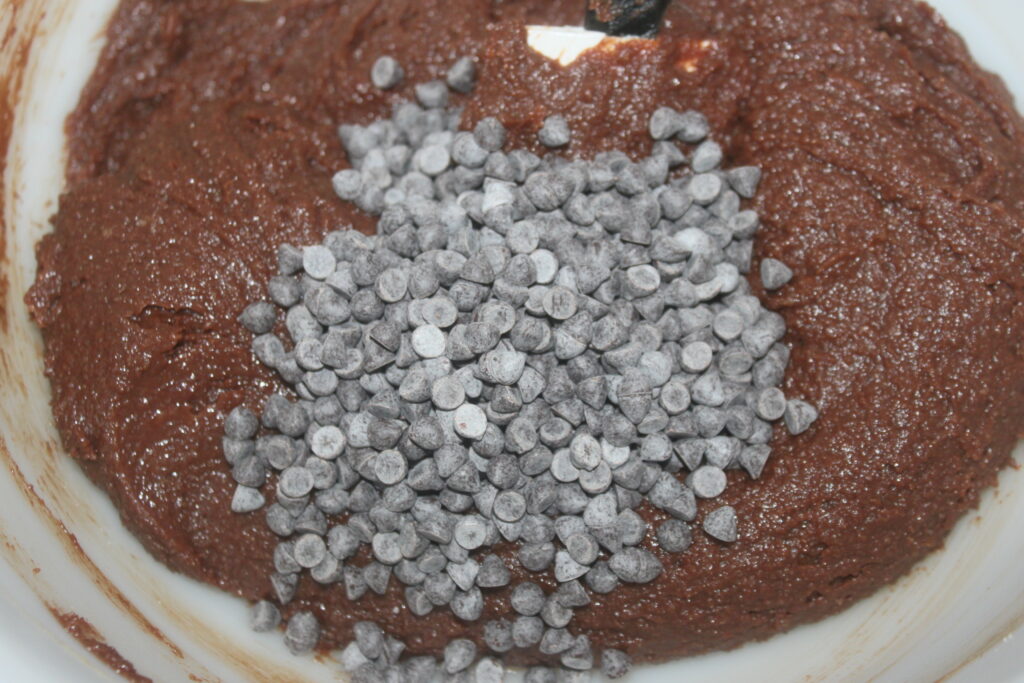 Gros plan d'une pâte à biscuits aux pépites de chocolat avec une pincée de pépites de chocolat sur le dessus dans un bol à mélanger, évoquant la riche essence d'un gâteau classique.