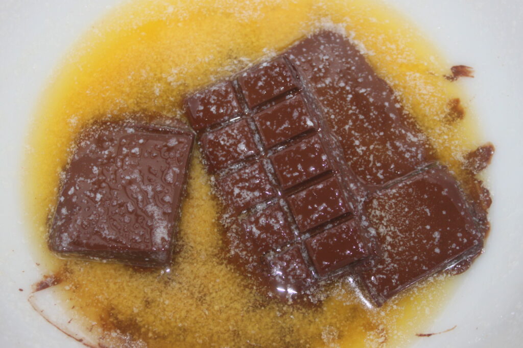 Dans un bol, deux barres de chocolat partiellement fondues se mélangent au beurre, créant la base parfaite pour votre chef d'œuvre de gâteau au chocolat.
