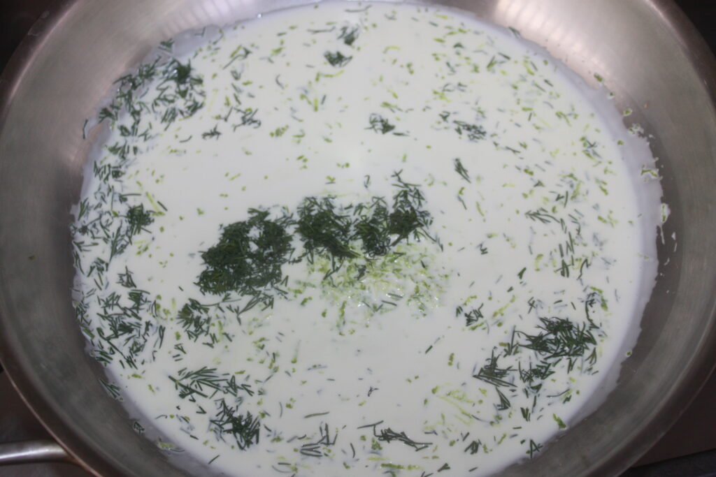 Une poêle remplie d'une sauce blanche crémeuse et d'un mélange parsemé d'herbes hachées, éventuellement d'aneth.