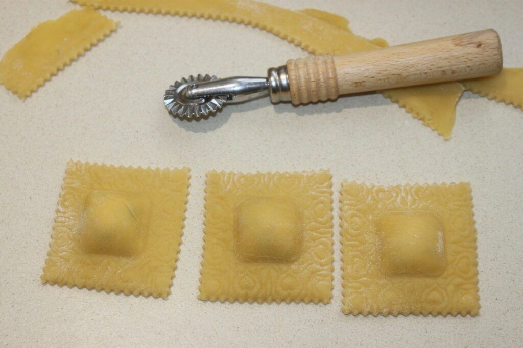 Trois raviolis à la ricotta crus reposent sur un comptoir, accompagnés d'un coupe pâtes à manche en bois.