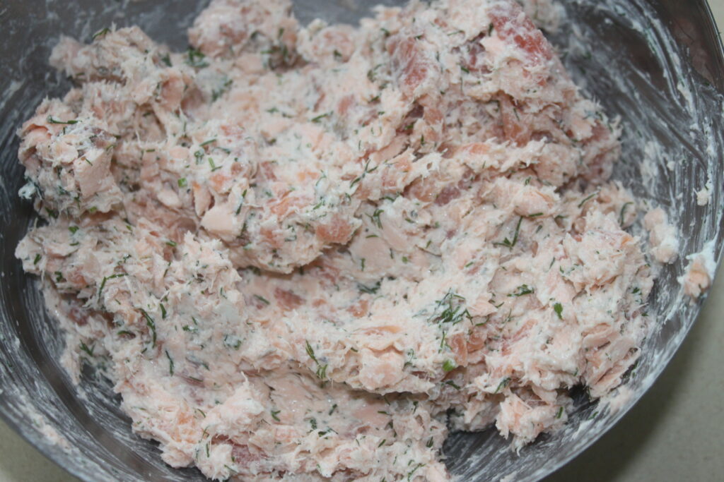 Gros plan d'un bol en métal contenant un mélange de viande hachée crue avec des herbes et des épices, rappelant une garniture de raviolis.