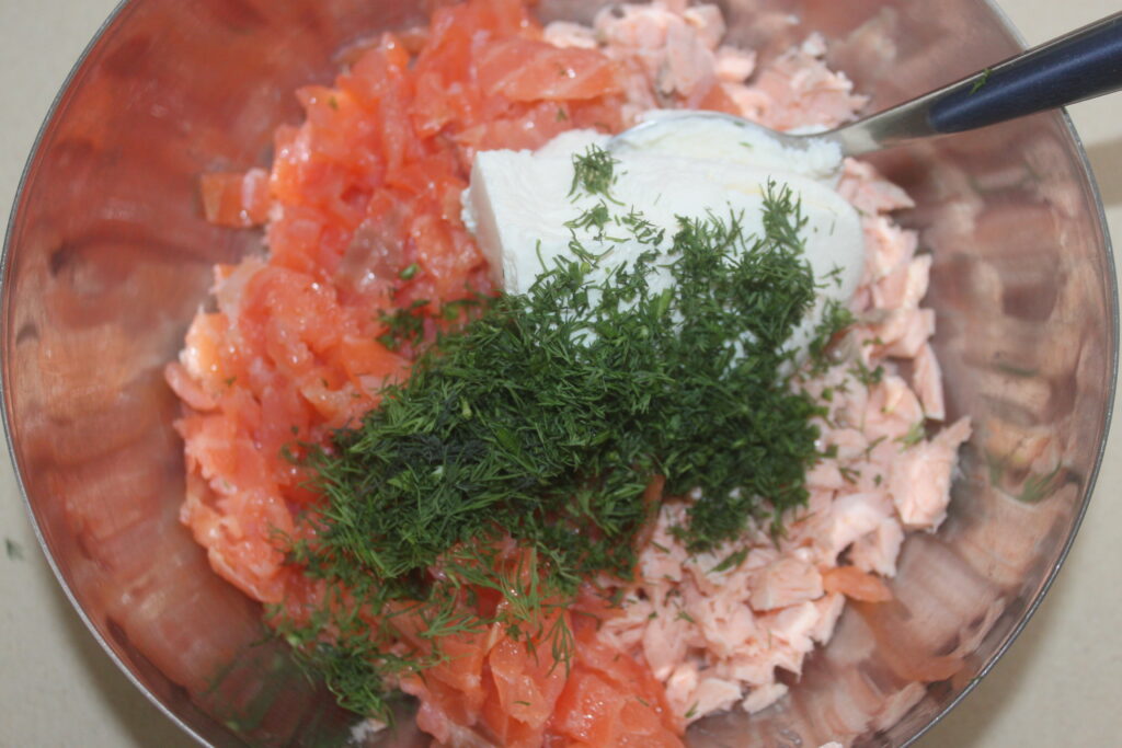 Un bol contenant du saumon haché, une cuillerée de crème, de l'aneth frais et une cuillère posée sur le côté évoque une combinaison exquise rappelant de délicats raviolis farcis de ricotta crémeuse.