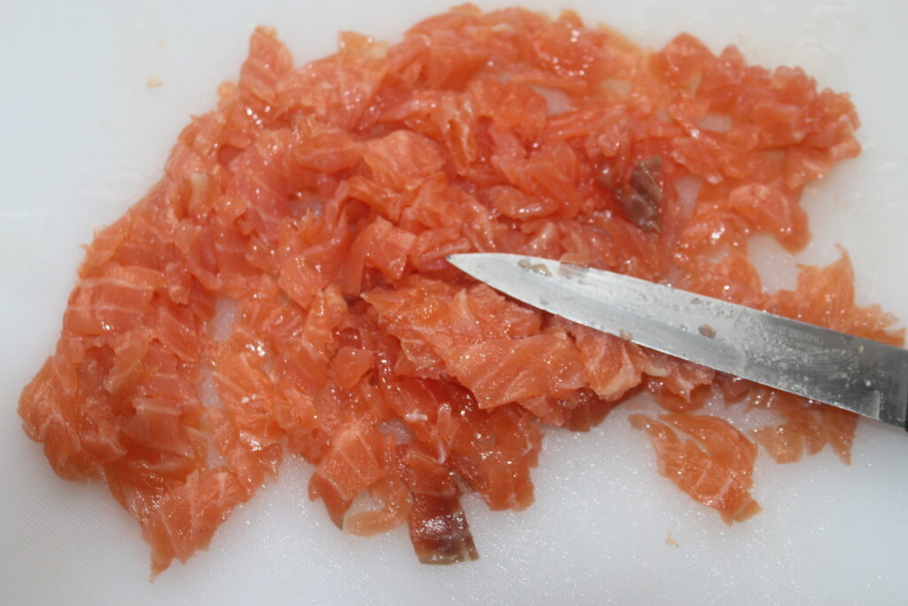 Saumon cru haché au couteau sur une planche à découper blanche.